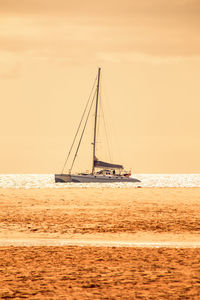 A catamaran with sails down, anchored in wonderful orange yellow evening glow in a bay