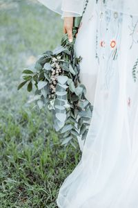 Low section of woman holding bouquet while standing on grass