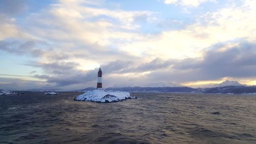 Lighthouse on island against cloudy sky