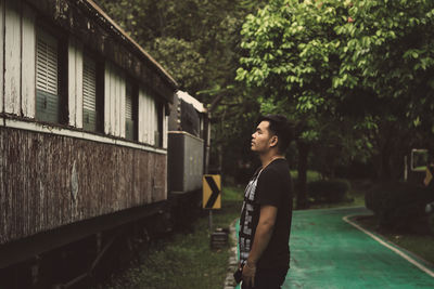 Side view of young man looking at old train while standing on footpath in park