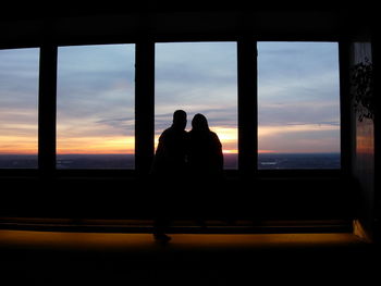 Silhouette couple looking through window at sunset