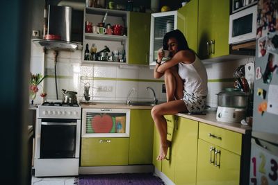 Side view of woman drinking coffee while sitting at kitchen 