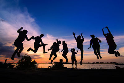 Silhouette people jumping on beach against sky during sunset