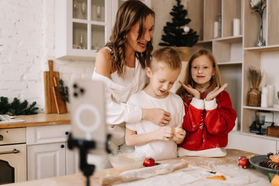 Mom, daughter and son prepare festive christmas food according to the recipe using a mobile phone