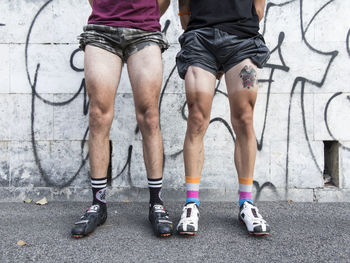 Low section of people in shorts standing on road against wall