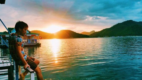 Woman sitting on lake against sky during sunset