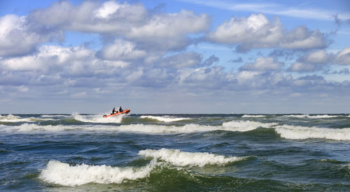 People sailing speedboat in sea against cloudy sky
