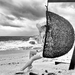 Full length of woman in hat sitting on beach chair