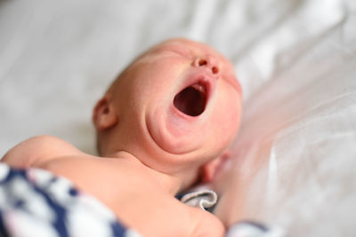 Close-up of baby boy yawning on bed