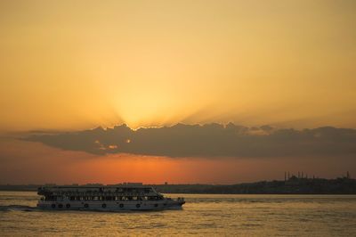 Silhouette boat sailing in sea against orange sky