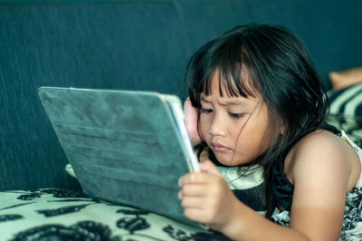 Little girl with digital tablet on the sofa.