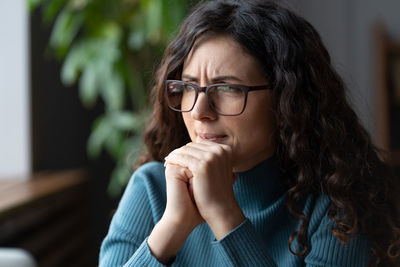 Young worried female employee in glasses feeling anxious, irritable or depressed at workplace