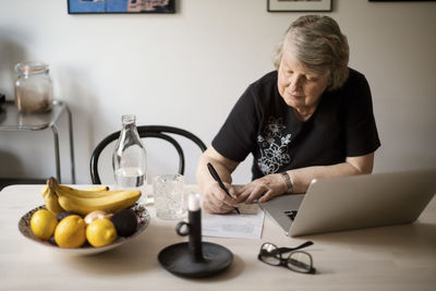 Senior woman checking for bills while using laptop at table
