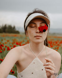 Attractive young woman sitting in the poppy field with flowers