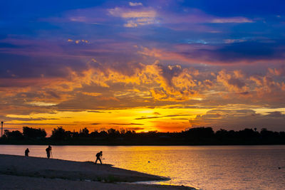 Silhouette people on beach against sky during sunset