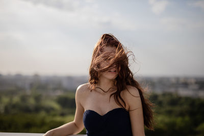 Young woman with tousled hair standing against sky