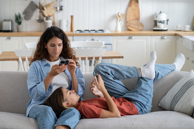 Friendly introverted family of woman mom and teenage girl using phone sits on sofa in living room