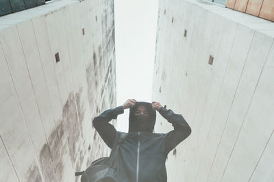 Low angle portrait of man wearing hood standing against buildings