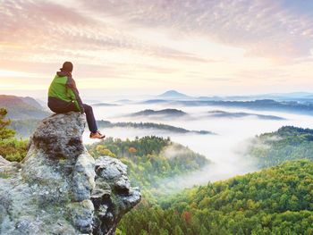 Hiker man take a rest on mountain peak. man sit on sharp summit and enjoy spectacular view.