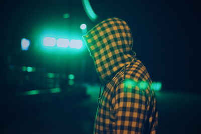 Side view of man wearing hooded shirt against green illuminated light