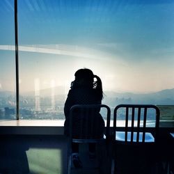Silhouette woman sitting on chair by sea against sky