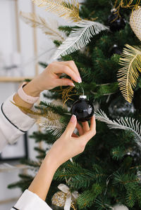 Woman's hand and ornaments on a beautiful christmas tree black toy ball.