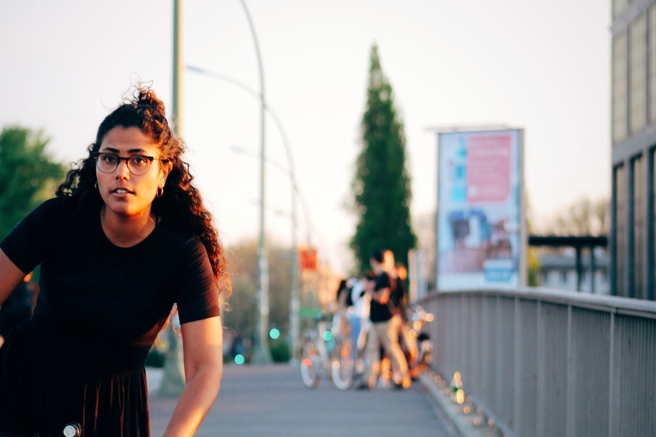 one person, real people, glasses, portrait, young adult, focus on foreground, front view, lifestyles, looking at camera, leisure activity, young women, sunglasses, casual clothing, fashion, standing, hair, architecture, women, outdoors, hairstyle, contemplation
