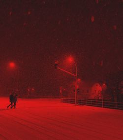 People walking on illuminated road against sky at night during winter