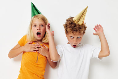 Portrait of smiling sibling wearing party hat against white background