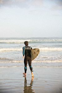 Rear view of man with surfboard running at sea shore against sky