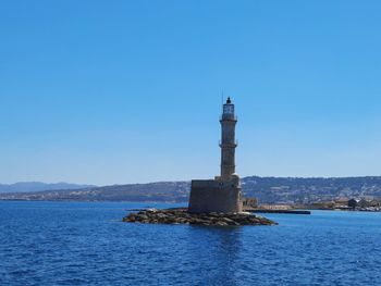 Lighthouse by sea against clear sky