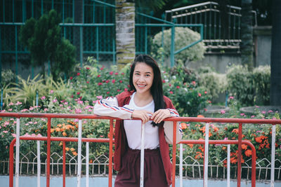 Portrait of smiling young woman standing against railing