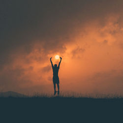 Silhouette man with arms raised standing on field against sky during sunset