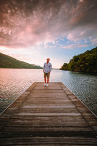 Rear view of man standing on pier over lake against sky