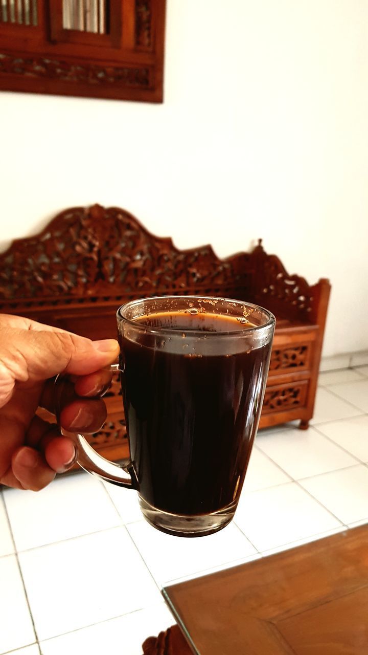 HAND HOLDING COFFEE CUP ON FLOOR