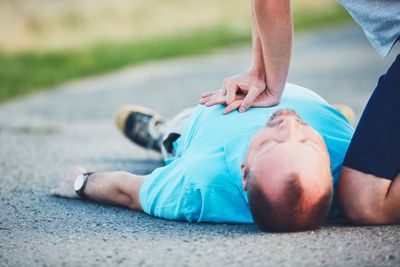 Midsection of man resuscitating friend lying on road