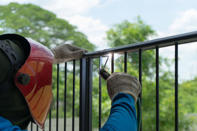 Close-up of hand holding railing against sky