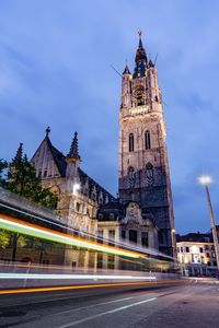 Light trails on street by church against sky during dusk