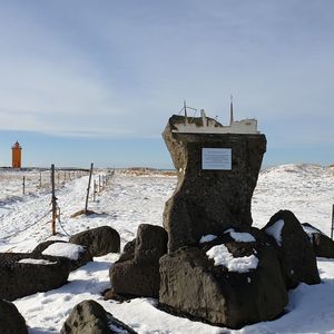 Cross on rock by sea against sky during winter