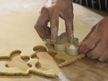 Cropped hands of chef cutting dough with pastry cutter at table