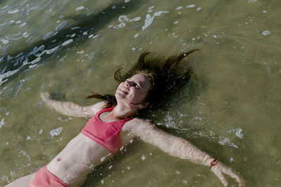 Girl lying down in water at beach on sunny day