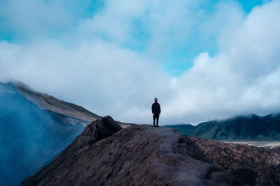 Young man standing on mountain against cloudy sky