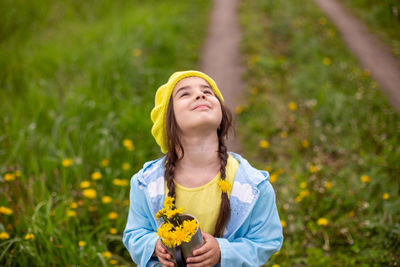 Portrait of a beautiful little girl holds a bouquet of yellow dandelions in a metal mug