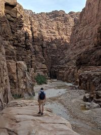 A man in the distance walking in the arid canyon of wadi mujib where a stream of water flows.