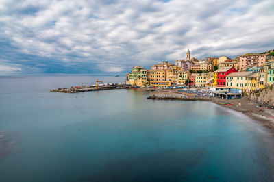 Buildings at waterfront against cloudy sky