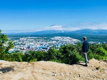 Rear view of man looking at city against blue sky