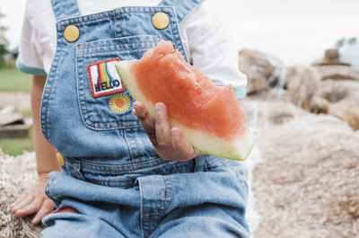 Midsection of girl holding bitten watermelon while sitting at farm