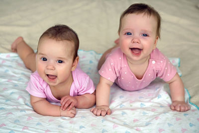 Two sisters twins baby in pink clothes lying on the bed in a diaper