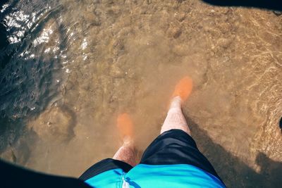 Low section of man standing in water on lakeshore