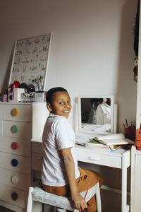 Side view of boy looking over shoulder while sitting at table in study room